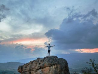 Man in prayer standing on top of rock mountain during golden hour.