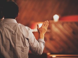 Person raising hand in prayer from behind.