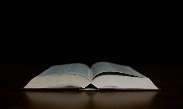 An open bible sitting on top of a wooden table.
